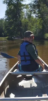 Person canoeing on a peaceful river surrounded by trees.