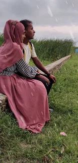 Couple sitting in nature with cloudy sky.