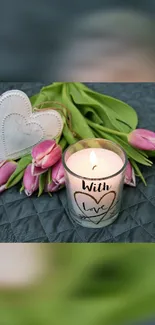 Candle with pink tulips and heart-shaped decor on a grey background.