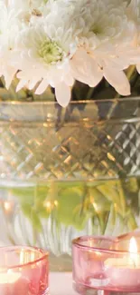 White flowers in vase with candles glowing softly.