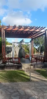 Sunlit garden with wooden pergola and bell structure.