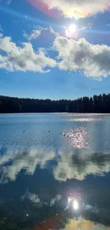 Serene lake under blue sky with cloud reflections and forest backdrop.