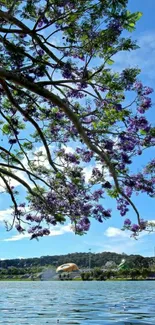 Purple flower branches over a tranquil lake under a bright blue sky.