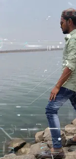 Man stands on rocky lakeside, admiring tranquil water.