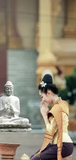 Woman in traditional attire praying before a Buddha statue in a temple setting.