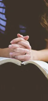 Person meditating with folded hands over a book, evoking peace and mindfulness.