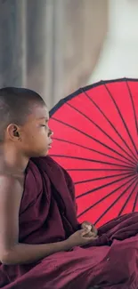 Young monk sitting in meditation with red umbrella.