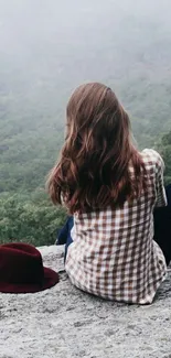 Person sitting on rock in misty green landscape, relaxing and serene.