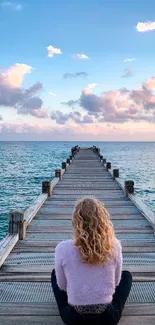 Person sitting on a pier facing a calm ocean under a beautiful sunset.