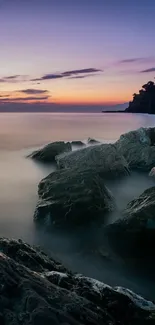 Serene sunset over rocky ocean shore with twilight sky.