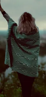 Silhouette of a person wrapped in a teal blanket overlooking nature.