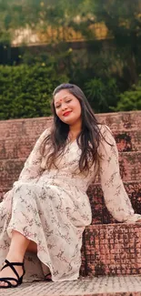 Woman in floral dress sits on rustic steps surrounded by greenery.