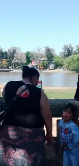 Woman and child by a calm riverside under a clear blue sky.