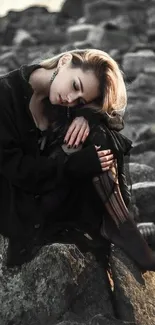 Woman in black outfit sitting on rocks by the shore, conveying calm and serenity.