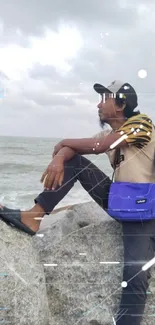 Person sitting on rocks by the ocean with a cloudy sky backdrop.