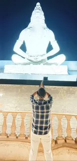 Man admiring a luminous Shiva statue at night.