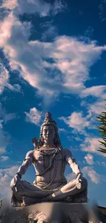 Statue of Shiva against a blue sky with clouds, evoking peace.