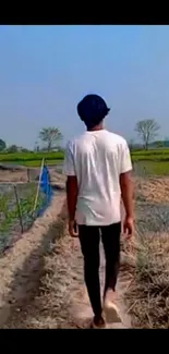 Person walking along a rural path under a clear blue sky.