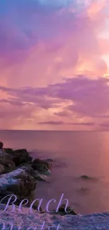 Purple sunset over ocean with rocky beach.