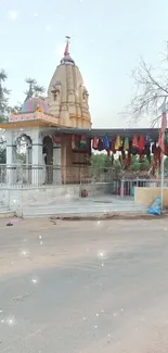 A serene roadside temple with trees and clear sky.