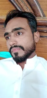 Man in white shirt relaxing indoors with wooden backdrop.