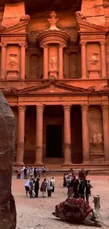 People and camels outside Al-Khazneh in Petra, pink sandstone at sunset.