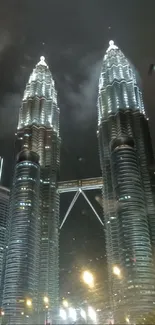 Petronas Towers illuminated at night, seen from a city street with cars.