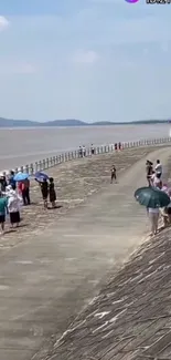 Scenic seaside walkway with people enjoying the beach view under umbrellas.