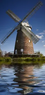 Windmill reflecting in a serene pond under a clear blue sky.