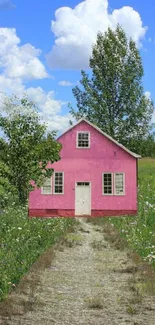 Pink cottage on a green field with a blue sky background wallpaper.