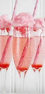 Three champagne flutes with pink cotton candy on top and pink striped straws.