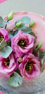 Top view of a pink cake with purple flowers and eucalyptus leaves on pink background.