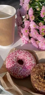 Donuts and pink flowers with coffee on a table.