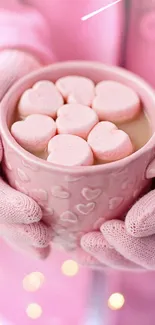 Hands holding a pink mug with heart-shaped marshmallows.