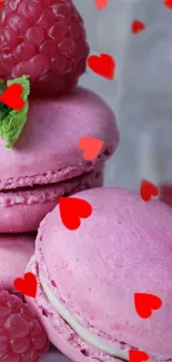 Pink macarons adorned with raspberries and red hearts.