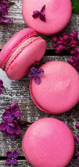 Pink macarons among purple flowers on wood.