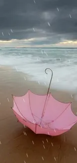 Pink umbrella resting on a sandy beach with ocean waves.