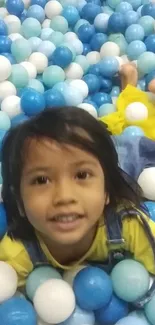 Child smiling joyfully amidst colorful play balls in a ball pit.