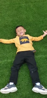 Child in yellow shirt lying on green grass, smiling contently.