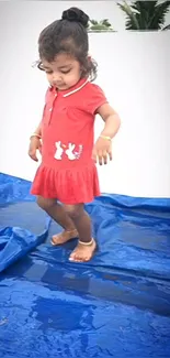 Girl in red dress standing on a blue tarp.