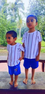 Children playing outdoors in lush greenery with matching outfits.