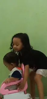 Two kids playing in front of a green wall, capturing a joyful moment.