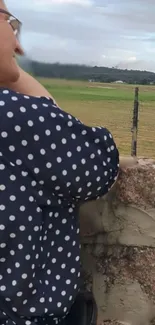 Woman in polka-dot shirt overlooking a serene countryside landscape.