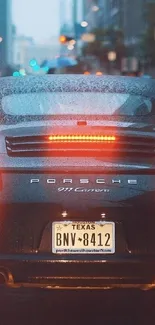 Rear view of Porsche 911 in a rainy city setting with glowing tail lights.