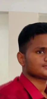 Young man in a red shirt with a neutral expression indoors.