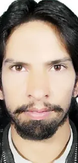 Close-up portrait of a bearded person with a neutral expression on a white background.