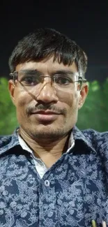 Man in glasses with green leafy background.