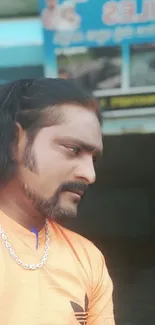 Man in orange shirt with thoughtful expression.