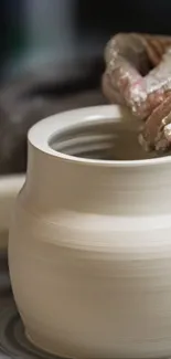 Hands shaping clay on a potter's wheel with beige tones.