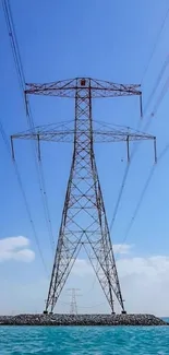 Towering powerline under a clear blue sky over turquoise water.